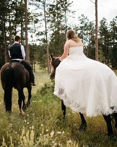 Bride and groom riding to their wedding ceremony on horseback at one of the most affordable colorado wedding venues